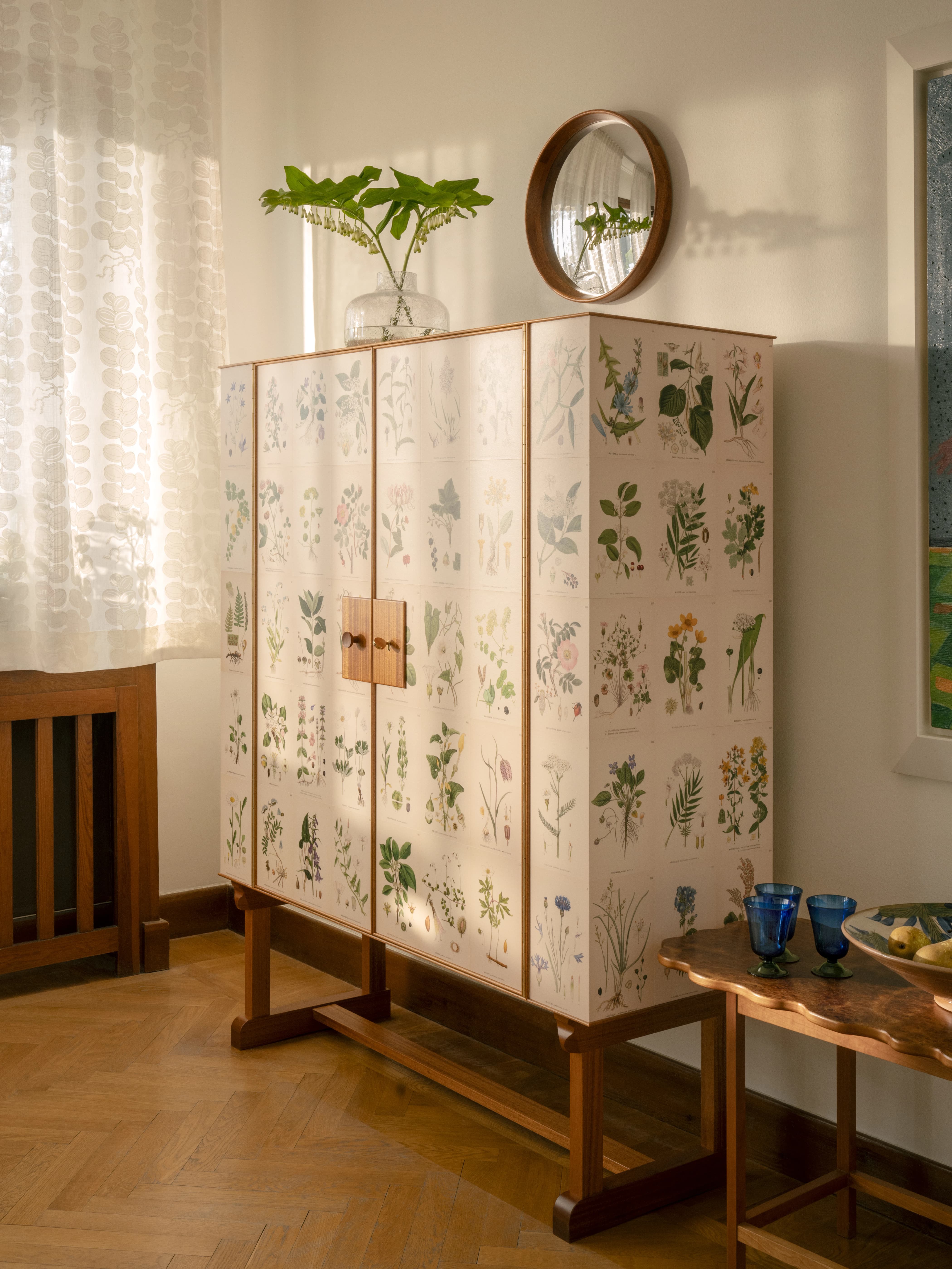 Botanical print cabinet in a bright room with a plant on top.